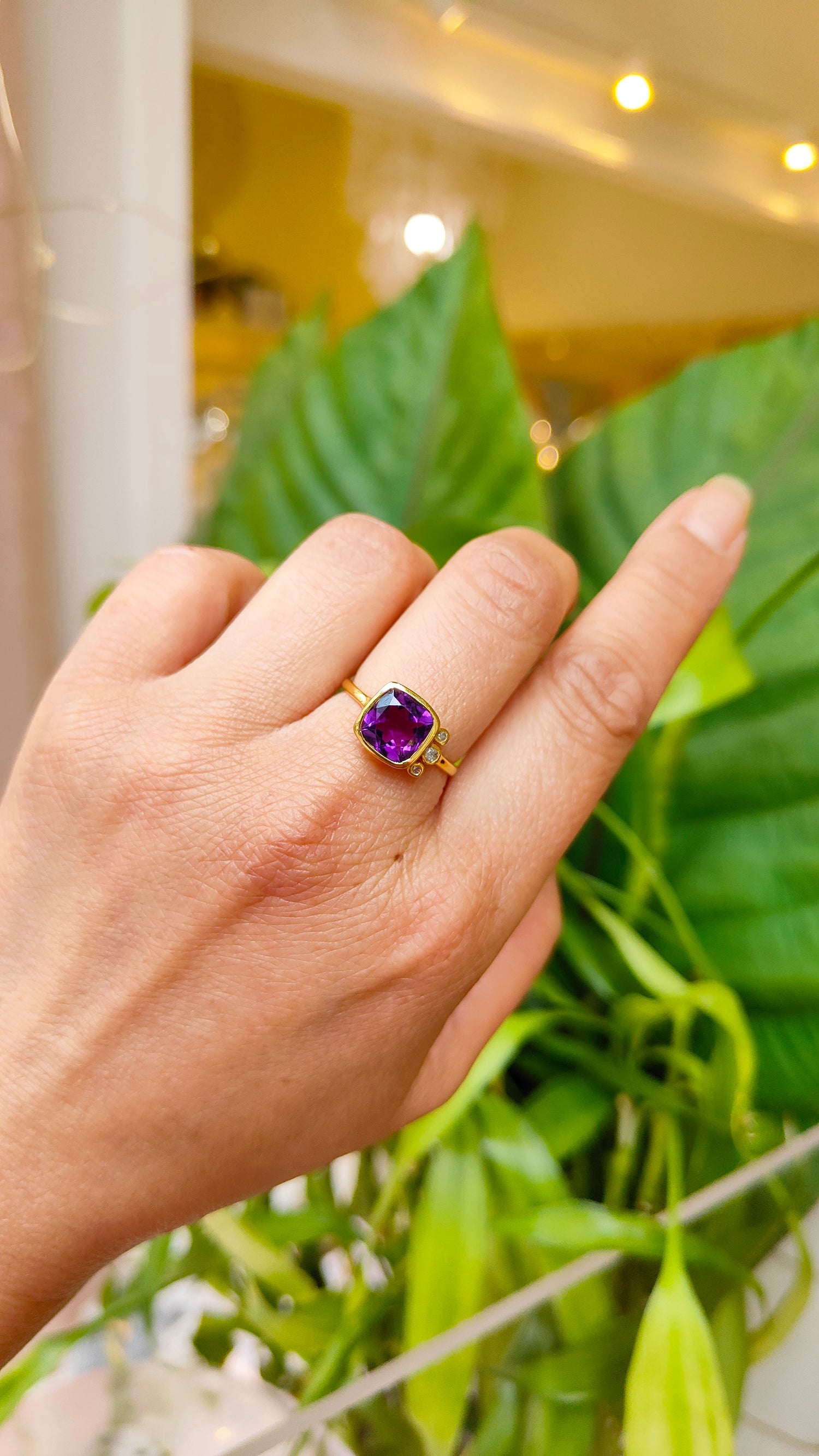 bague en améthyste et diamant portée sur une main avec un fond de plantes